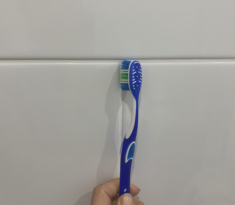 using an old toothbrush to clean bathroom grout